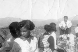 A group of five young adults sitting on the ledge at Panorama Point with hills and mountains in the background, 1955 circa.