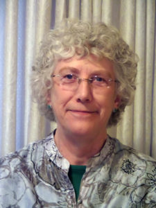 Portrait of a mature woman with curly gray hear wearing glasses.